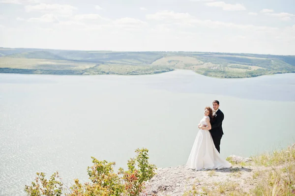 Hochzeitspaar in atemberaubender Landschaft mit Fels und See. — Stockfoto