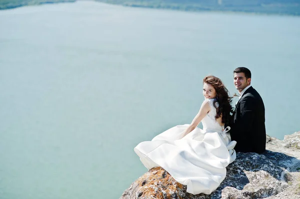 Wedding couple at breathtaking landscape with rock and lake. — Stock Photo, Image