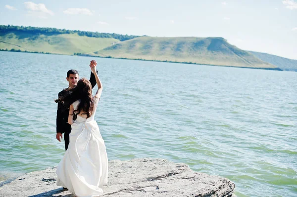 Wedding couple at breathtaking landscape with rock and lake. — Stock Photo, Image