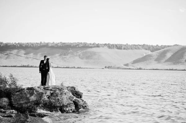 Wedding couple at breathtaking landscape with rock and lake. — Stock Photo, Image