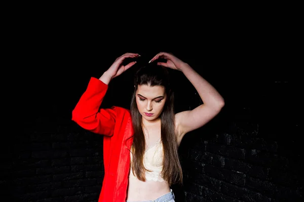 Stijlvolle brunette meisje op rode jas tegen studio zwarte baksteen w — Stockfoto