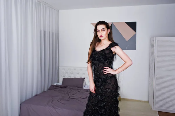 Bruna ragazza in abito da sera nero contro camera bianca con letto — Foto Stock