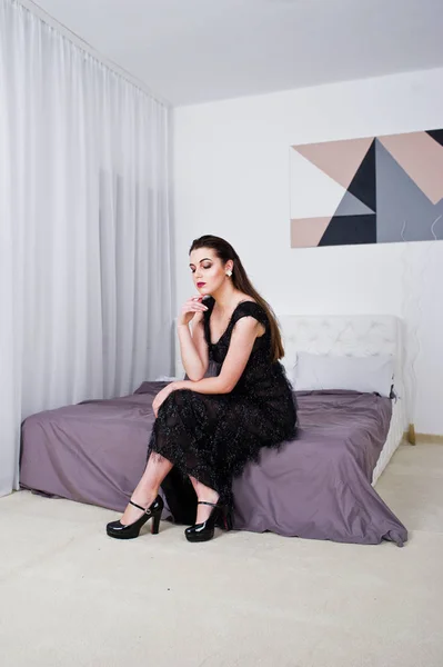 Brunetka dziewczyna w czarnej sukni przeciwko białym pokoju z łóżkiem — Zdjęcie stockowe