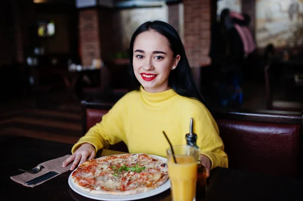 Lucu gadis berambut cokelat dengan sweater kuning makan pizza di restoran — Stok Foto