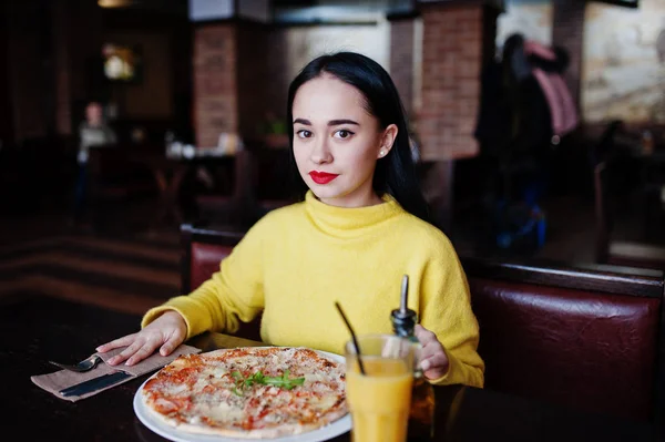 Смешная брюнетка в желтом свитере ест пиццу в ресторане — стоковое фото