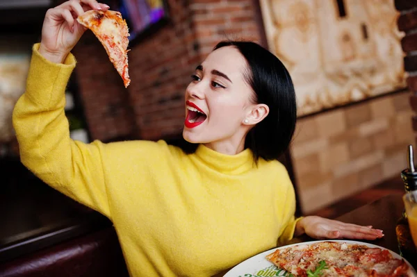 Zabawna Dziewczyna Brunetka w żółty sweterek jedzenie pizza w restauracji — Zdjęcie stockowe