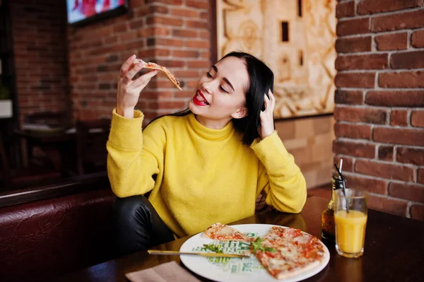 Смешная брюнетка в желтом свитере ест пиццу в ресторане — стоковое фото