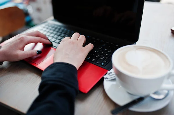 Ellerini kızın cappu fincan ile kırmızı dizüstü bilgisayar ile çalışma kapatın — Stok fotoğraf