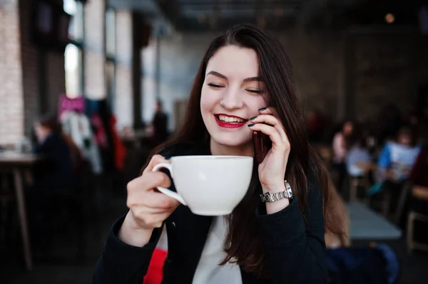 Chica morena sentada en la cafetería con taza de capuchino y speakin — Foto de Stock