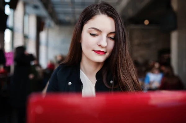 Chica morena sentada en la cafetería y trabajando con el ordenador portátil rojo . — Foto de Stock