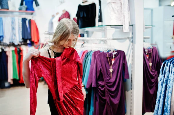 Chica rubia intenta un vestido rojo en la boutique . — Foto de Stock