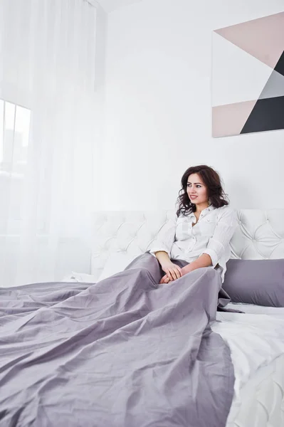 Πορτραίτο στούντιο μελαχρινή κοπέλα σε λευκή μπλούζα ξαπλωμένος στο κρεβάτι. — Φωτογραφία Αρχείου