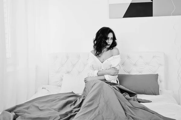 Studio portret van brunette meisje in witte blouse liggend op bed. — Stockfoto