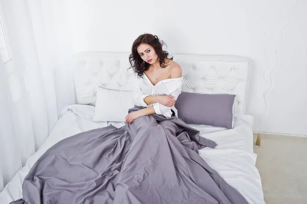 Studio portret van brunette meisje in witte blouse liggend op bed. — Stockfoto