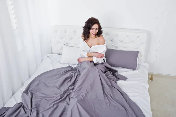Portret Studio brunetka dziewczyna w białej bluzce, leżąc na łóżku. — Zdjęcie stockowe