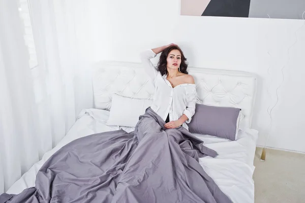 Studioporträt eines brünetten Mädchens in weißer Bluse, das auf dem Bett liegt. — Stockfoto