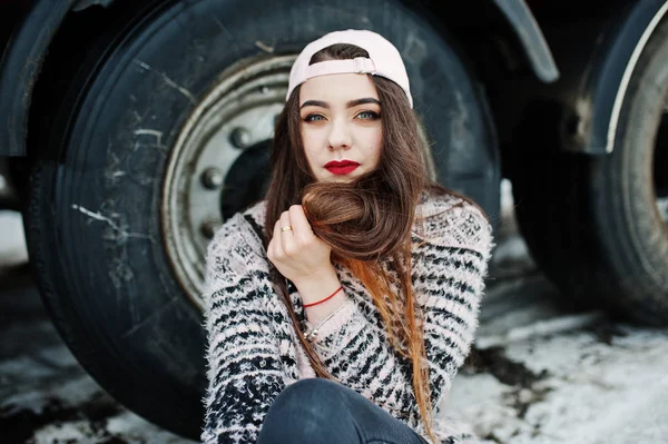 Брюнетка стильная девушка в кепке сидит против колеса грузовика — стоковое фото