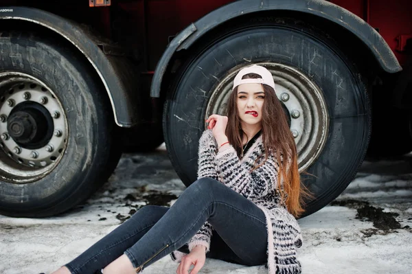 Morena elegante casual menina em cap sentado contra rodas de caminhão — Fotografia de Stock