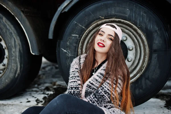 Brunette stylish casual girl in cap sitting against truck wheels — Stock Photo, Image