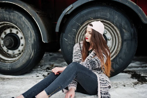 Morena elegante chica casual en la tapa sentado contra ruedas de camiones —  Fotos de Stock