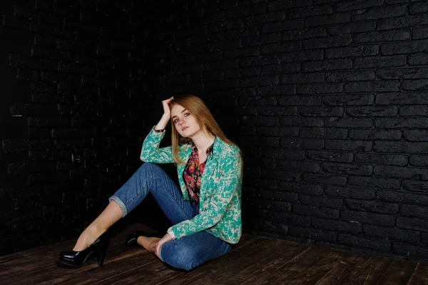 Menina loira elegante na jaqueta e jeans contra parede preta de tijolo — Fotografia de Stock