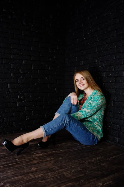 Stijlvolle blond meisje in jas en jeans tegen bakstenen muur black — Stockfoto