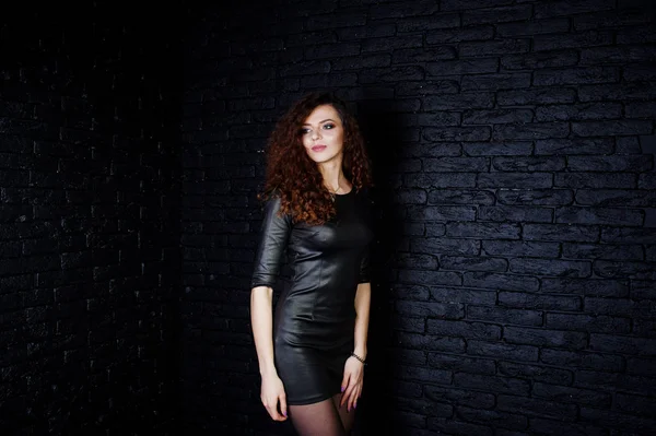 Brunette gekrulde haired lange benen meisje in zwart leer jurk pose — Stockfoto