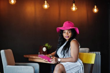 Ta oturan elinde tablet ile şapkalı Afrika kökenli Amerikalı kadın