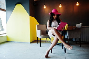 Ta oturan elinde tablet ile şapkalı Afrika kökenli Amerikalı kadın