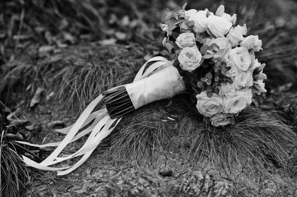 Wedding bouquet with white ribbons on grass.