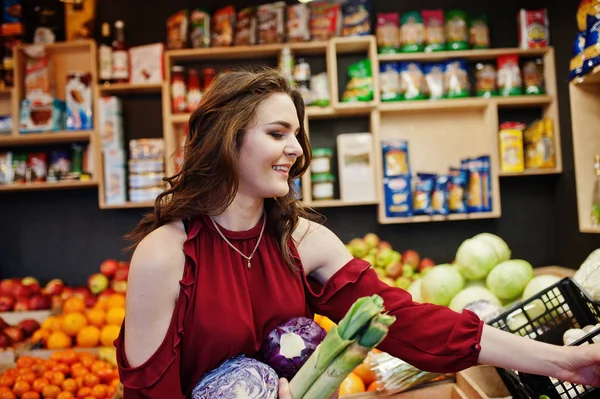 Dziewczyna w czerwonym posiadających różne warzywa w sklepie owoce. — Zdjęcie stockowe