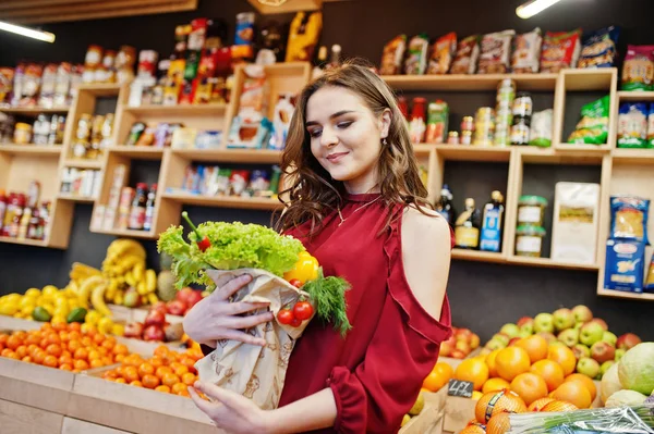 Dziewczyna w czerwonym posiadających różne warzywa w sklepie owoce. — Zdjęcie stockowe