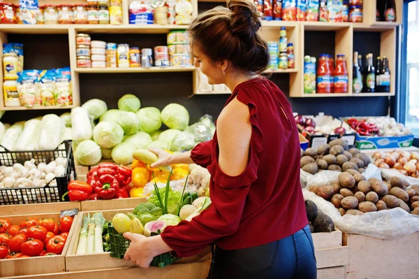 Дівчина в червоному тримає різні овочі в магазині фруктів . — стокове фото
