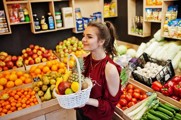 Дівчина в червоному тримає різні фрукти і овочі в кошику — стокове фото