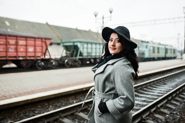 Brünettes Mädchen im grauen Mantel mit Hut im Bahnhof. — Stockfoto