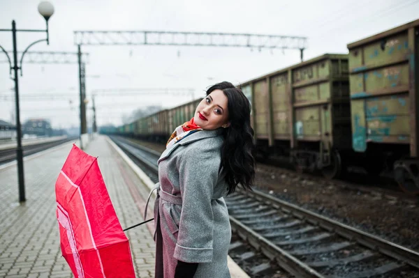 역에서 빨간 우산으로 회색 코트에 갈색 머리 소녀. — 스톡 사진