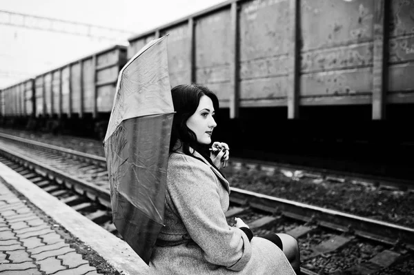 Brunette fille en manteau gris avec parapluie rouge dans la gare . — Photo