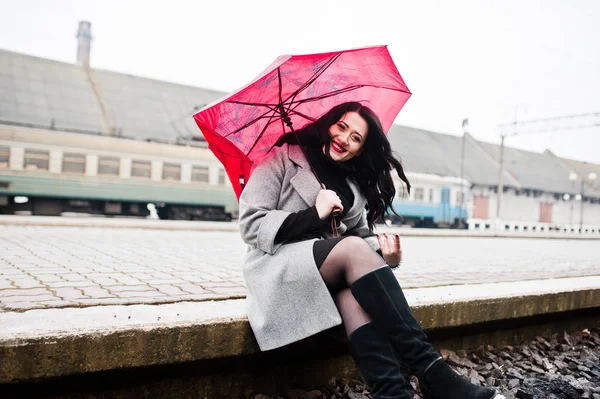 Brunette fille en manteau gris avec parapluie rouge dans la gare . — Photo