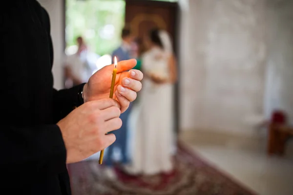 Las manos del hombre con vela en la iglesia contra la pareja casada en casada — Foto de Stock