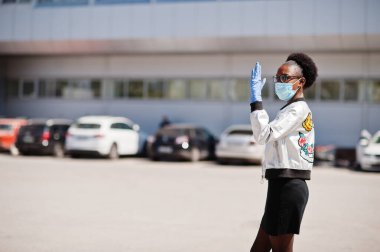 Tek kullanımlık tıbbi maske takan Afrikalı kadın ve eldivenler salgın sırasında dışarıda yürüyor..