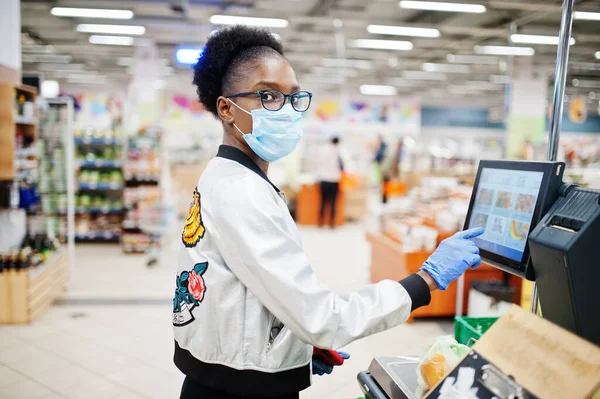 非洲妇女带着一次性医疗面罩和手套在超级市场购物 这是在腮腺炎爆发期间发生的 在流行病流行的时候 黑色的女性是水果的重量 — 图库照片