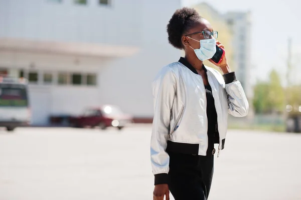 African woman wearing disposable medical mask and gloves walking outdoor and speaking phone during epidemic time.