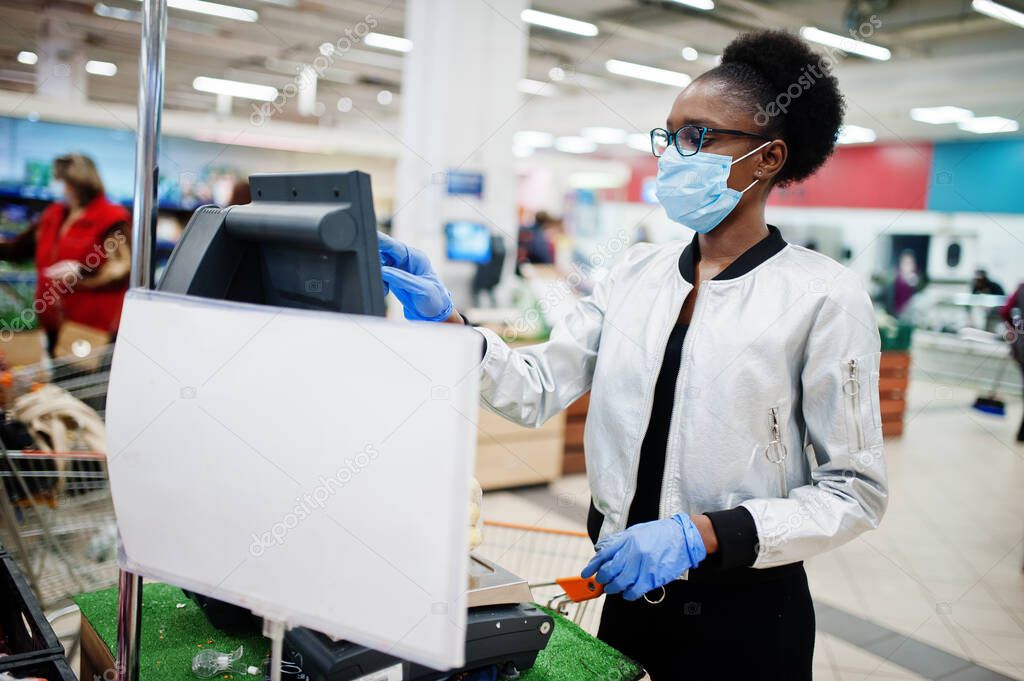 African woman wearing disposable medical mask and gloves shopping in supermarket during coronavirus pandemia outbreak. Black female weighs fruits at epidemic time.