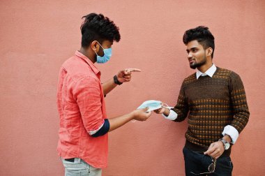 Coronavirus covid-19 konsepti. Pembe arka planda izole edilmiş Corona virüsünden korunmak için maske takan iki Güney Asyalı adam. Sosyal uzaklık.