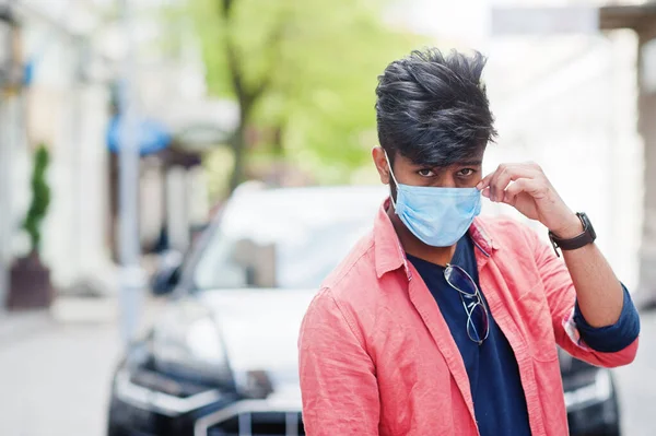 Coronavirus covid-19 concept. South asian indian man wearing mask for protect from corona virus posed against business car.