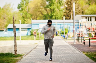 Siyah tıbbi maskeli Arap portresi Coronavirus karantinası sırasında açık havada koşar..