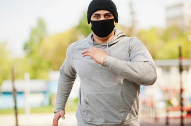 Siyah tıbbi maskeli Arap portresi Coronavirus karantinası sırasında açık havada koşar..