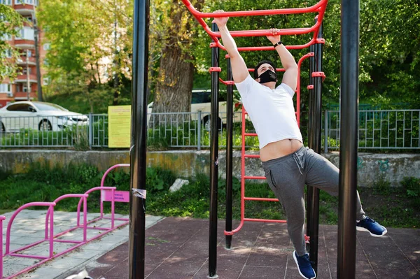 Portrait sports arabian man in black medical face mask doing workout exercises in outdoor gym place during coronavirus quarantine.