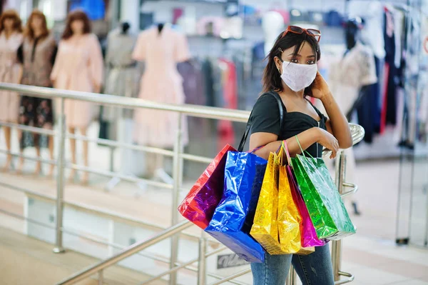 African american woman wearing face protective medical mask for protection from virus disease with shopping bags in mall during coronavirus pandemia.