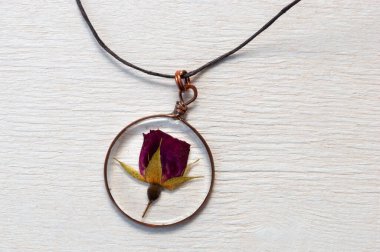 handmade epoxy resin jewelry. pendant, rose in copper frame. dried flowers. herbarium, oshibana, phytotherapy. on white wooden background clipart